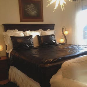 May include: A dark brown wooden bed frame with a glossy black duvet cover and matching black pillowcases. The bed is dressed with white ruffled pillows and a white bed skirt. Two curved gold lamps with textured glass shades sit on nightstands.