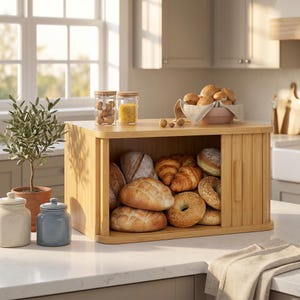 May include: A bamboo bread box with a sliding door, filled with various types of bread, including loaves, croissants, and bagels. The top shelf holds glass jars with food items and a bowl of bread. A small potted plant and ceramic jars are on the counter.