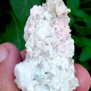 May include: Close-up of a mineral specimen featuring a cluster of light-colored crystals. The crystals are a pale, translucent color, with a rough, textured surface. The background is a blurred green.