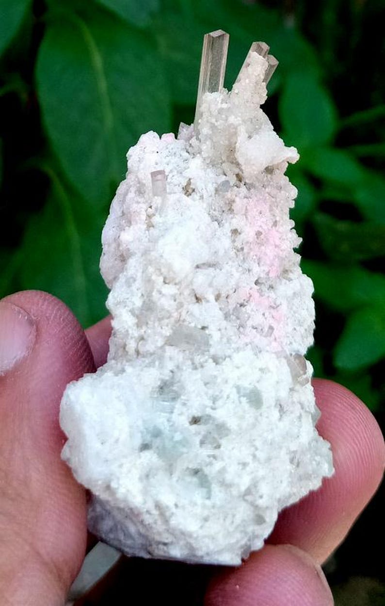 May include: Close-up of a mineral specimen featuring a cluster of light-colored crystals. The crystals are a pale, translucent color, with a rough, textured surface. The background is a blurred green.