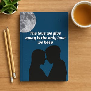 Puede incluir: Un cuaderno con una cubierta azul oscuro que presenta una silueta de dos personas abrazándose bajo un cielo iluminado por la luna. El texto "The love we give away is the only love we keep" está impreso en blanco. Dos lápices y una taza de té están sobre la superficie de madera.