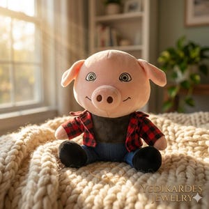 May include: A plush pig wearing a red and black plaid shirt, blue jeans, and black shoes. A gold bracelet with a pearl is in front of the pig. The pig is sitting on a cream-colored knitted blanket. The text "YEDIKARDES JEWELRY" is at the bottom right.