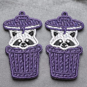 May include: Two embroidered patches featuring a white and black raccoon peeking out from inside a purple trash can with a matching purple lid. The raccoon has black eye patches, black ears, and a small black nose, all rendered in detailed thread work.