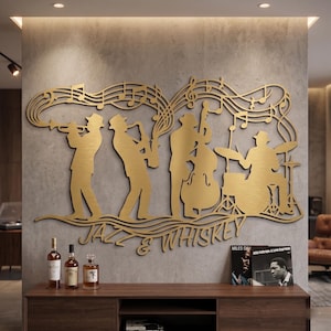 Op de afbeelding: Een goudkleurig metalen wandkunstwerk dat een jazzband afbeeldt die instrumenten bespeelt, met muzieknoten die boven hen stromen. De woorden "JAZZ & WHISKEY" staan onder de band. Flessen drank en een Miles Davis-album staan op een houten kast.
