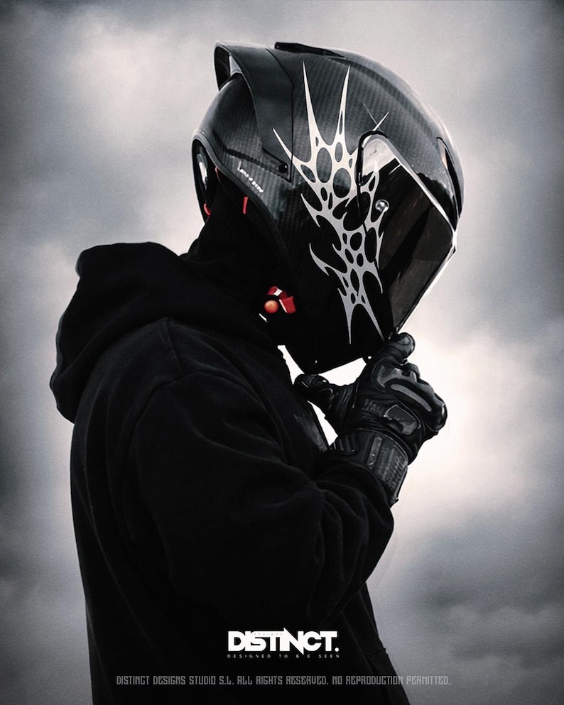May include: A black motorcycle helmet with a white tribal design. The helmet has a dark visor and is worn with black gloves and a black hoodie. The image includes the text "DISTINCT. DESIGNED TO BE SEEN."