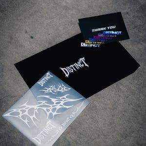 May include: A collection of stationery items featuring the word "DISTINCT" in a stylized font. The items include a black envelope, a translucent envelope, and a thank you card, all with the same branding. The background is a gray concrete surface.