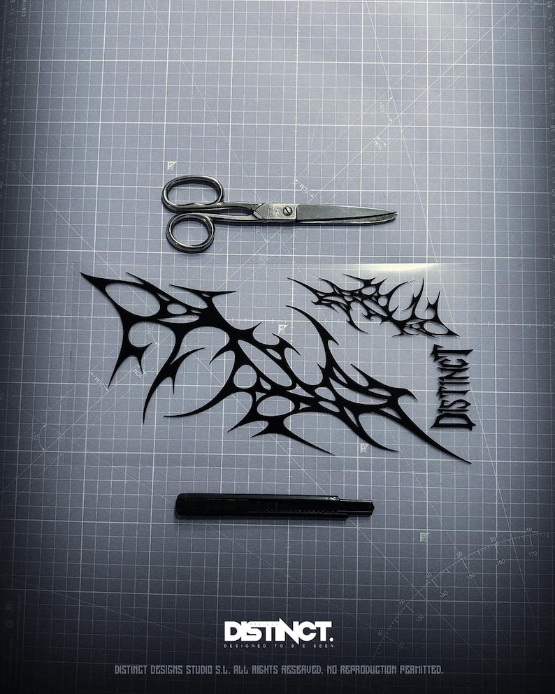 May include: A top-down shot shows a gray cutting mat with a pair of scissors, a black utility knife, and black tribal-style decals. The decals are in a spiky, abstract design. The word "DISTINCT" is printed on the bottom.