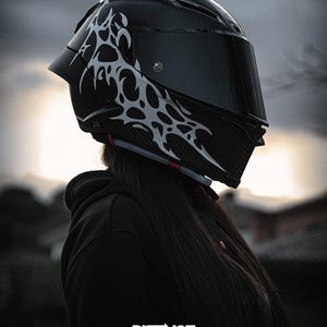 May include: A black motorcycle helmet with a dark visor and a white tribal design on the side. The helmet has a glossy finish and is designed for safety. The image includes the text "DISTINCT. DESIGNED TO BE SEEN."