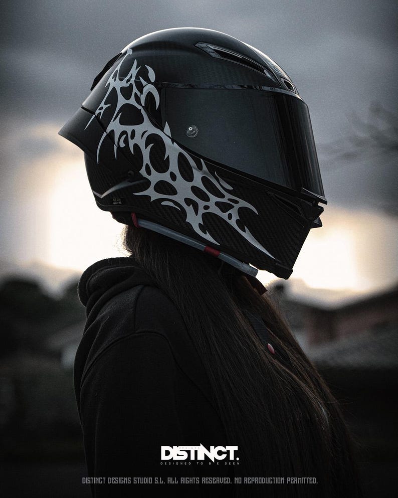 May include: A black motorcycle helmet with a dark visor and a white tribal design on the side. The helmet has a glossy finish and is designed for safety. The image includes the text "DISTINCT. DESIGNED TO BE SEEN."