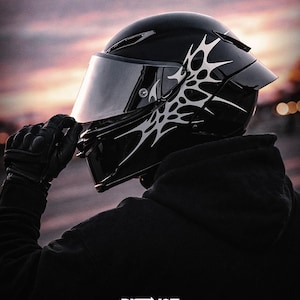 May include: A glossy black motorcycle helmet with a silver tribal design on the side. The helmet has a tinted visor and is held by a gloved hand. The word "DISTINCT" is printed at the bottom.