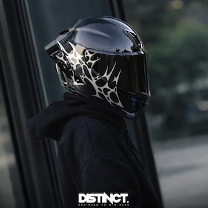 May include: A glossy black motorcycle helmet with a dark visor and a white, abstract design on the side. The helmet is part of a motorcycle gear collection. The text "DISTINCT. DESIGNED TO BE SEEN" is visible at the bottom.