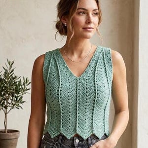 Könnte beinhalten: Ein ärmelloses, mintgrünes Häkeltop mit V-Ausschnitt. Das Top hat ein detailliertes Lochmuster und einen gewellten Saum. Die Frau trägt eine dunkelblaue Jeans.