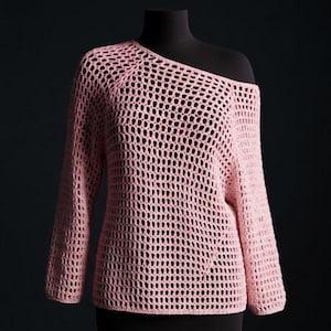 May include: A light pink, open-weave sweater with a one-shoulder neckline and long sleeves. The sweater is displayed on a black mannequin against a dark background. The knit design features large, evenly spaced holes.