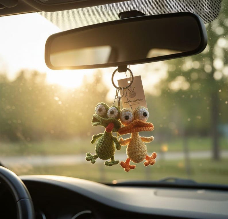 Puede incluir: Dos amuletos de coche hechos a mano, de ganchillo, cuelgan de un espejo retrovisor. Uno es una rana verde, el otro es un pato naranja. Ambos tienen ojos grandes y saltones y est&aacute;n unidos a un llavero con una peque&ntilde;a etiqueta que dice "Handmade Charm".