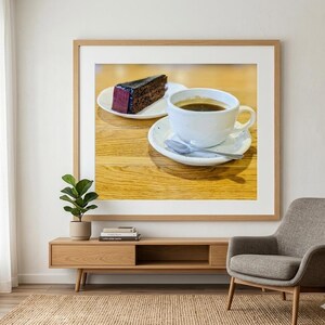 Könnte beinhalten: Gerahmtes Bild mit einem Stück Schokoladenkuchen mit lila Glasur auf einem weißen Teller und einer weißen Kaffeetasse mit Kaffee auf einer Untertasse mit einem Löffel. Die Gegenstände stehen auf einem Holztisch.