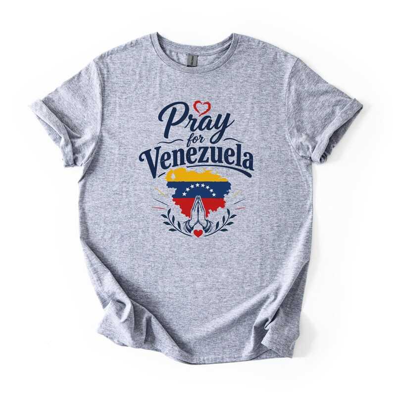 May include: A heather gray short-sleeve t-shirt featuring the dark blue text Pray for Venezuela above a map of Venezuela filled with the national flag colors of yellow, blue, and red, with a pair of praying hands and small red hearts.