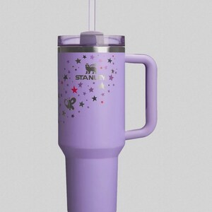 May include: A lavender Stanley tumbler with a handle and a straw. The tumbler is decorated with a pattern of stars and butterflies. The Stanley logo is visible on the side.
