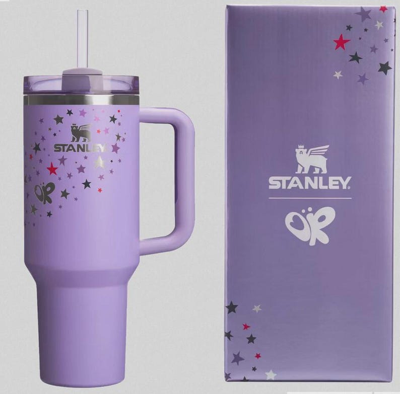 May include: A lavender Stanley tumbler with a handle, straw, and lid. The tumbler is decorated with silver stars and the Stanley logo. The matching box features the Stanley logo and star accents.