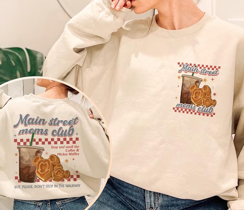 Pu&ograve; includere: Felpa color crema con la scritta "Main street moms club" in blu e rosso. Il design include una tazza di caff&egrave; e waffle di Mickey Mouse. Il retro della felpa ripete il design con la scritta "Stop and smell the Coffee & Mickey Waffles."