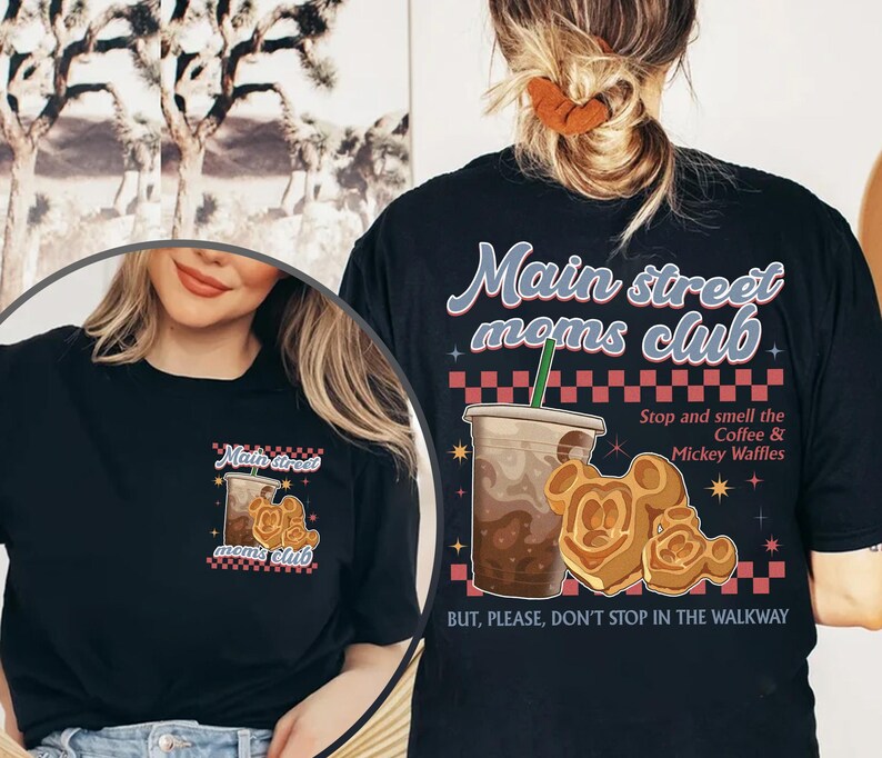 Pu&ograve; includere: T-shirt nero con la scritta "Main Street Moms Club" e grafica. Il design include una tazza di caff&egrave;, waffle di Mickey Mouse e la frase "Stop and smell the Coffee & Mickey Waffles."