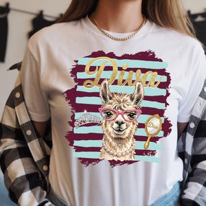 Puede incluir: Camiseta blanca con una llama con gafas rosas y un collar de perlas, con la palabra "Diva" en letras doradas. El diseño incluye una tiara y un espejo de mano. El fondo tiene rayas burdeos y turquesas.