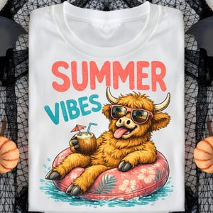 Könnte beinhalten: Weißes T-Shirt mit den Worten "SUMMER VIBES" in Koralle und Türkis. Die Grafik zeigt eine Cartoon-Hochlandkuh mit Sonnenbrille, die auf einem rosa Blumen-Schwimmring schwimmt und ein Kokosnussgetränk hält.