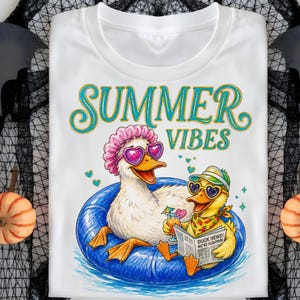 Op de afbeelding: Wit t-shirt met een kleurrijke afbeelding van twee eenden die van de zomer genieten. Eén eend draagt een roze badmuts en hartvormige zonnebril, de andere een hoed en zonnebril, lezend een krant met de kop "Duck News! We're Floating!". De woorden "Summer Vibes" staan erboven.