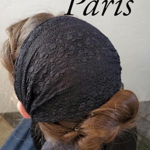 May include: Black lace headband with the word "Paris" in script. The headband is worn on the head, covering the forehead and top of the head. The hair is pulled back and styled in a braid.