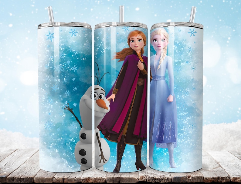 Puede incluir: Tres vasos de acero inoxidable con pajitas, con personajes de la pel&iacute;cula animada "Frozen". Los dise&ntilde;os incluyen a Anna, Elsa y Olaf sobre un fondo azul nevado con acentos de copos de nieve. Los vasos est&aacute;n sobre una superficie de madera.