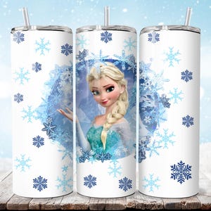 Puede incluir: Un vaso blanco con un dise&ntilde;o de Elsa de Frozen, rodeado de copos de nieve azules. El vaso tiene una tapa plateada y una pajita transparente. El dise&ntilde;o incluye un retrato de Elsa con un vestido azul y turquesa.