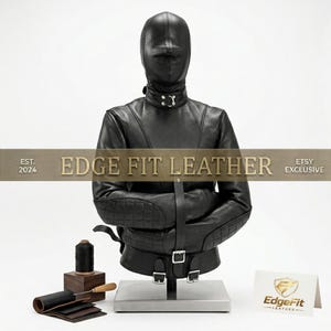 Può includere: Una camicia di forza in pelle nera con cappuccio integrale abbinato, dotata di gomitiere trapuntate, fibbie color argento e un anello sul colletto. Il testo EDGE FIT LEATHER EST. 2024 ETSY EXCLUSIVE è sovrapposto. Un rocchetto di filo e campioni di pelle sono vicini.