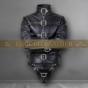 May include: A black leather garment featuring a high collar, a central zipper, and multiple horizontal straps secured with silver-toned metal buckles and rivets. The text "EST. 2024 EDGE FIT LEATHER ETSY EXCLUSIVE" is overlaid across the center.