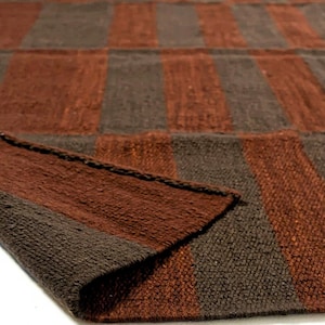 May include: A woven rug with a checkerboard pattern of alternating brown and dark brown stripes. The rug's edge is folded over, revealing the texture of the material. The rug appears to be made of natural fibers.