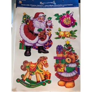 May include: A sheet of removable window stickers featuring a Santa Claus figure, a brown teddy bear holding a stack of gifts, a rocking horse, a purple Christmas ornament, and gold bells. The text reads Removable Window Stickers.