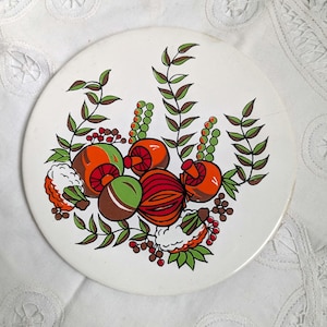 Peut inclure: Une assiette décorative ronde blanche avec un motif botanique coloré. L'illustration comprend des fruits et des feuilles stylisés orange, rouges, verts et bruns. L'assiette a une esthétique vintage.