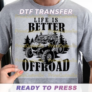 May include: A gray t-shirt with a black graphic that reads "LIFE IS BETTER OFFROAD." The design includes a detailed illustration of an off-road vehicle and pine trees. The words "DTF TRANSFER" and "READY TO PRESS" are also visible.