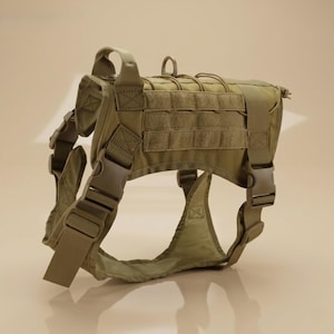 May include: A tan dog harness with multiple adjustable straps and buckles. The harness features a series of MOLLE webbing for attaching additional pouches or accessories. A handle is located on the top of the harness.