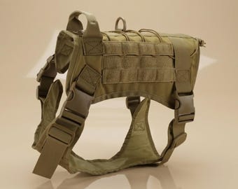 Puede incluir: Un arnés táctico para perro de color beige que cuenta con un asa superior reforzada, una anilla en D de metal para la correa, hebillas laterales ajustables y paneles de correas MOLLE en los laterales para fijar equipo modular.