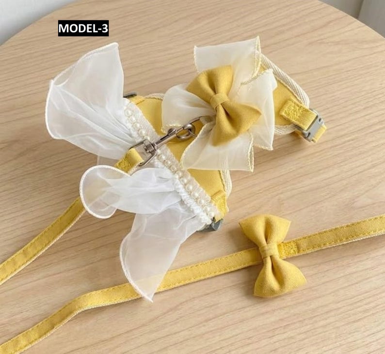 Puede incluir: Un arn&eacute;s para mascota etiquetado como MODEL-3 con volantes de organza blanca transparente, una hilera de peque&ntilde;as perlas blancas y un lazo de tela amarilla. El arn&eacute;s incluye una correa amarilla a juego con un peque&ntilde;o lazo de tela amarilla.