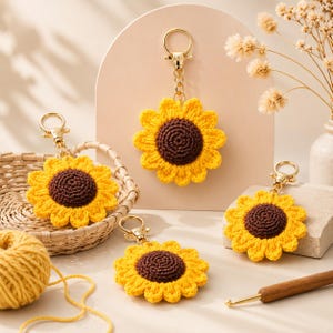 May include: Four handmade crochet sunflower keychains with gold-colored hardware. The sunflowers have yellow petals and brown centers. One keychain is in a woven basket, and a ball of yellow yarn and a crochet hook are also visible.