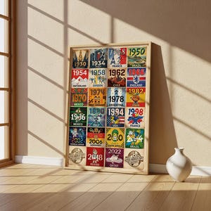 May include: A framed print featuring a collage of FIFA World Cup posters from 1930 to 2022. Each poster showcases the year, host country, and a unique design. The print is in a light wooden frame, with a white vase in the background.