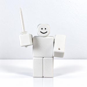 以下が含まれることがあります： シンプルな黒いスマイリーフェイスが描かれた丸い頭部を持つ、白いブロック型のフィギュア。四角い胴体、2本の長方形の脚、2本のブロック状の腕がある。片方の手には上を向いた白い剣を持ち、もう片方の手には長方形の盾を持っている。