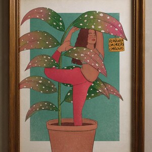 Pode incluir: Impressão artística emoldurada com uma mulher em pose de ioga, integrada com uma planta em vaso. A mulher usa leggings e top rosa, com as folhas da planta a rodeá-la. A obra de arte tem uma paleta de cores verde e rosa, com uma pequena etiqueta na planta.