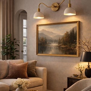 May include: A living room scene featuring a beige sofa with decorative pillows, a round wooden coffee table, and a framed landscape painting. Above the painting, a brass and white double-light fixture provides illumination. The room has a neutral color palette.