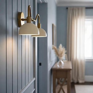 May include: Cream-colored wall sconces with a brass finish are mounted on a blue paneled wall. The sconces have a curved design and are positioned near a doorway. The room has a neutral color palette with a wooden console table.