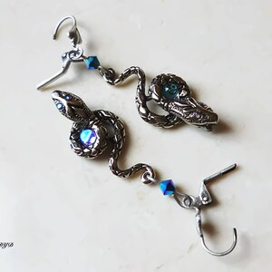 K&ouml;nnte beinhalten: Silberne Schlangenohrringe mit blauen, schillernden Kristall-Akzenten. Die Schlange ist aufgerollt und hat ein detailliertes Design.