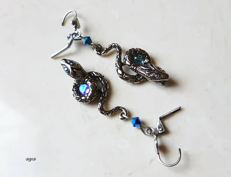 K&ouml;nnte beinhalten: Silberne Schlangenohrringe mit blauen, schillernden Kristall-Akzenten. Die Schlange ist aufgerollt und hat ein detailliertes Design.