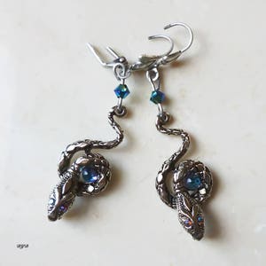K&ouml;nnte beinhalten: Ein Paar silberne Schlangenohrringe mit blauen, irisierenden Glasaugen. Die Ohrringe h&auml;ngen und haben einen Hakenverschluss.
