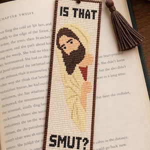 May include: A rectangular cross-stitch bookmark with a brown border and a matching brown tassel. The design features a figure with a beard and a light-colored robe, with the black stitched text IS THAT at the top and SMUT? at the bottom.