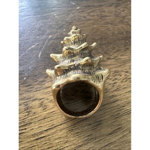May include: A gold-toned metal ring shaped like a spiraled seashell. The ring features a textured, conical design with layered ridges that taper toward the top, and a smooth, circular band opening at the base for a finger to pass through.